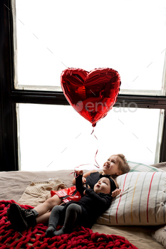 Sisters withhold a coronary heart-formed balloon of their hand whereas lying on the mattress.