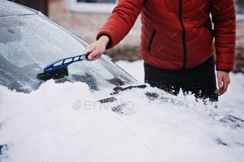 Man cleansing vehicle from snow and ice with brush and scraper instrument right by snow fall. Frosty weather emergency