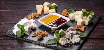 Several forms of cheese on a shale tray with mint and candy sauces