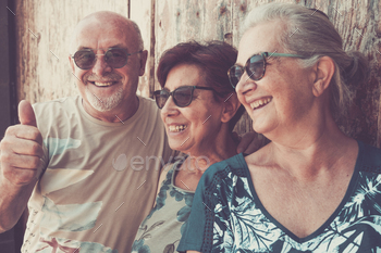 Three elderly folk standing against a wooden door laughing, opinion of senior pensioner holidays