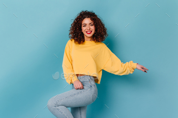 Blue-eyed lady with intriguing lips and snow-white smile is posing on blue background. Girl in yellow s