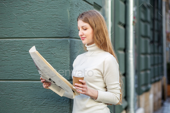 Busy girl with newspaper and takeaway coffee in a single hand stands on road. Rhythm of huge city.