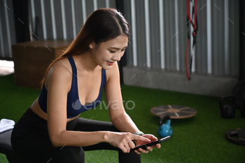 Younger asian girl in sportswear  taking a atomize after after practising sport and the employ of fresh phone.