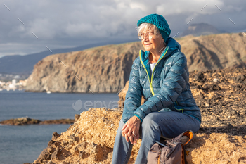 Portrait of senior smiling girl in out of doorways tour at sea sitting on cliff attempting the horizon