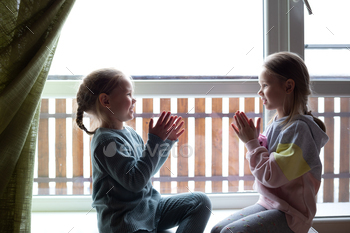 two ladies are playing patty-cake, sitting on the windowsill come the massive window