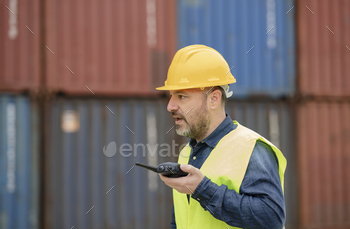 man with walkie talkie and helmet working within the port with logistics containers