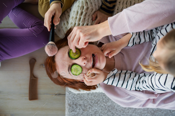 Exiguous chidlren putting cucumber on their mother’s face and applying assemble up to her at dwelling