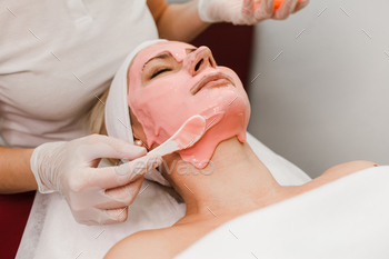 Physician beautician applies anti-increasing old masks to lady face. Ladies lies on a cosmetology direction of.