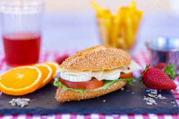 Sesame seed sandwich with cheese, tomatoes and laborious boiled egg on murky stone cutting board