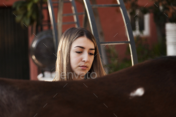 Younger blonde lady alongside with her brown horse enjoys a day on the farm.