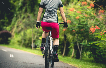 Woman no handed cycling on tropical park slouch in summer season