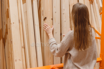 Lady picking wooden plank in ironmongery shop. Building materials for dwelling renovation