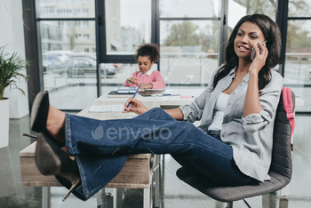 smiling businesswoman talking on smartphone whereas daughter doing homework