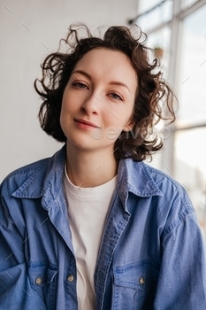 Cease-up portrait of smiling young girl with short curly hair in blue shirt having a stare at digicam