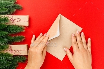 process sending letter to Santa Claus in craft envelope on red background with Christmas decorations