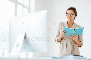 Young darkish haired girl in smooth set aside on holds blue notepad focused into video display