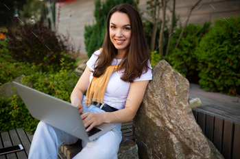 adorable younger feminine pupil sitting with notebook computer on lunch destroy sitting out of doorways