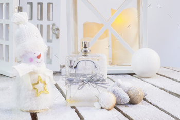 a bottle of heady scent tied with a festive ribbon on a snowy wooden surface with balloons with cones