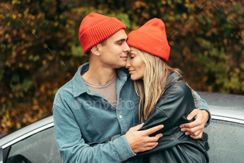 Younger man and lady in crimson caps hugging originate air in autumn.