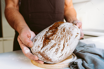 Rye craft hand-crafted bread in muscular textured hands of male baker