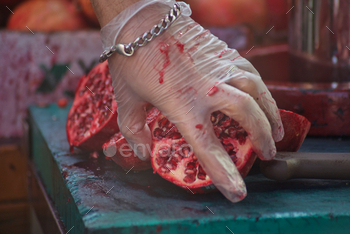 Pomegranates on a decreasing board with blood esteem juice on unrecognizable gloved hand