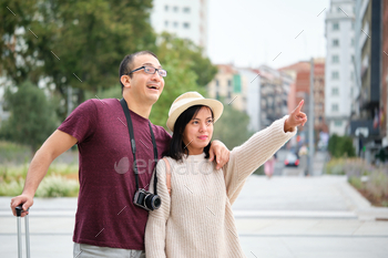 Chuffed multiracial couple of guests exploring the metropolis collectively and pointing.