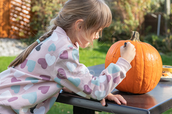 Small lady attracts eyes and mouth on Halloween pumpkin with marker