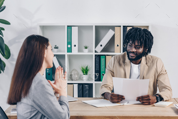 Selective focal level of worker with praying hands  recruiter smiling with papers at table in