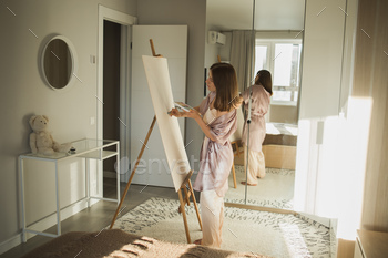 Younger woman artist painting on canvas on the easel at home in mattress room – artwork and creativity theory