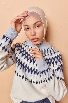 Portray of Islamic girl touches face gently looks to be like straight at camera with restful expression wears hijab