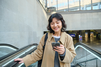 Technology and folks thought. Smiling brunette lady travels around metropolis, holds smartphone and