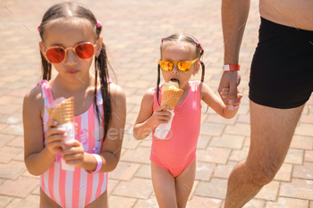 A father leads his young daughters to the beach.