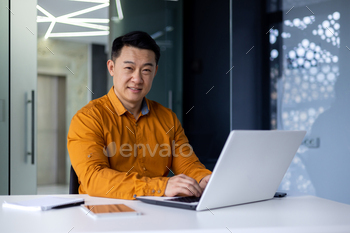 Portrait of overjoyed and satisfied asian programmer inside space of work working with pc pc, male freelancer