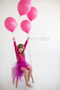 Humorous kid girl celebrating birthday with balloons in room over white