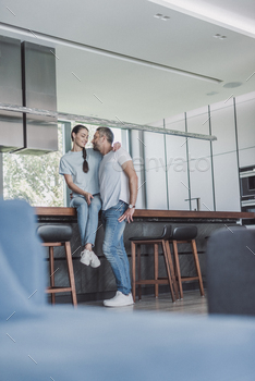 low perspective survey of dazzling woman sitting on kitchen counter and embracing boyfriend at dwelling