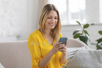 Elated millennial caucasian blonde female in yellow garments study message on smartphone, chatting