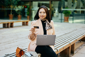 Asian businesswoman using pc whereas paying online with bank card and  digicam.