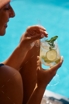 Pack up of lady having mojito cocktail by swimming pool.