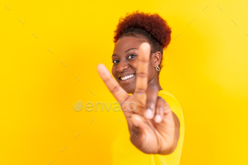 Younger african american girl isolated on a yellow background smiling with the victory gesture