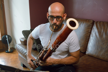 front peer of young classical song composer man, taking part in bassoon studying sheet song at dwelling