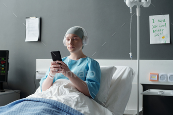 Young ill woman with oncological disease the order of smartphone in clinical institution ward