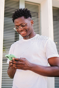 Vertical portrait of smiling young african american man the usage of his smartphone for messaging in social