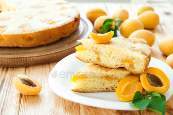 Piece of apricot pie on plate with plump cake and apricot fruits.