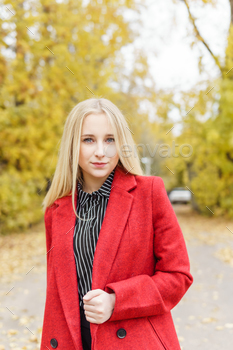 A younger blonde girl walks right via the autumn city in a red coat. The opinion that of city fashion