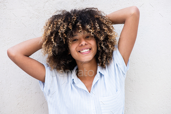 chuffed younger african american lady with fingers in hair by white wall