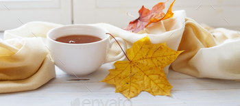 autumn leaves with a cup of tea or coffee subsequent to a scarf on a wood background banner