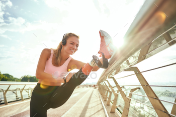 Disabled particular lady in sportswear and headphones stretching prosthetic leg whereas standing on