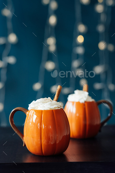 Pumpkin fashioned cups of hot drink with whipped cream, cinnamon stick on gloomy table and sad