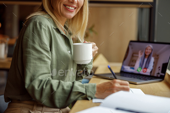 Close up of replace lady is drinking coffee and making notes all the design through video convention in coworking