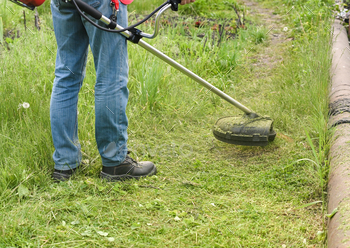 Worker mowing enormous grass with electric or petrol backyard trimmer in city park or yard.